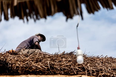 Téléchargez les photos : Dar es Salaam, Tanzanie - Mars 2022 : L'homme local est en train de réparer un toit de chaume. Photo de haute qualité - en image libre de droit
