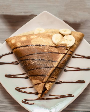 chocolate pancake with banana and chocolate sauce on wooden table