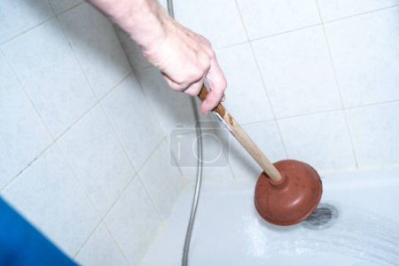 Foto de Person cleans the shower drain clogged sink with a plunger. Pipes clogged with waste and hair. Drain cleaning concept. House cleaning. - Imagen libre de derechos
