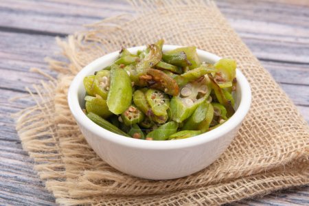 Grilled okra, in a white bowl on a wooden table, focused, isolated