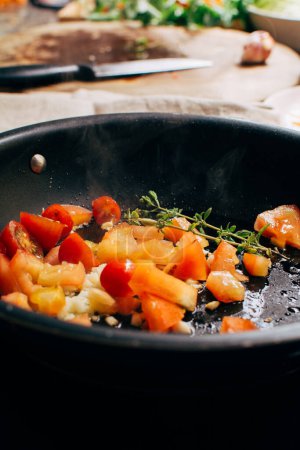Foto de Los tomates fritos y el ajo en la cacerola, la salsa para la pasta, la comida italiana que prepara con las hierbas, vertical - Imagen libre de derechos