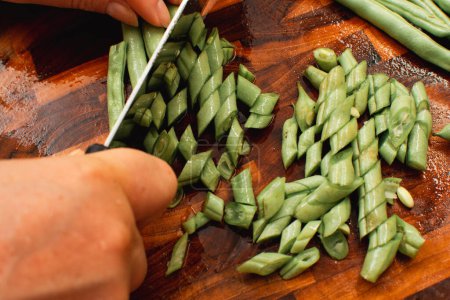 Foto de Foto de la mano femenina picando judías verdes en la tabla de cortar de madera para cocinar - Imagen libre de derechos