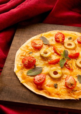Foto de Sartén de pizza casera con tomates, albahaca y aceitunas en un plato de madera en vista superior - Imagen libre de derechos