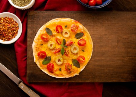 Foto de Sartén de pizza casera con tomates, albahaca y aceitunas en un plato de madera en vista superior - Imagen libre de derechos