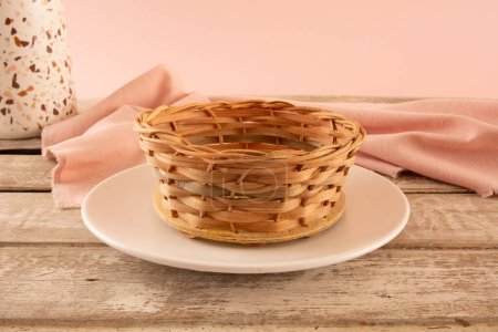 Photo for Empty bamboo basket in a pink background inside a gray ceramic plate above a wooden table - Royalty Free Image