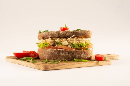 Foto de Sándwich de pechuga de pollo en pan de grano entero con ensalada fresca en una mesa de madera sobre un fondo blanco en vista frontal - Imagen libre de derechos