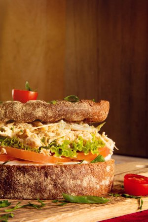 Foto de Sandwich de pechuga de pollo en pan de grano entero con ensalada fresca en una mesa de madera sobre un fondo de madera en vista frontal recortada - Imagen libre de derechos