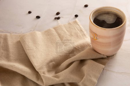 Coffee mug in a marbled stone background with beige napkin in front view