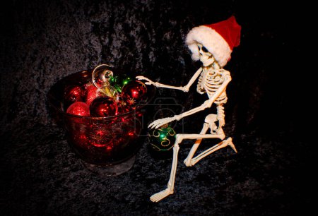 Foto de Esqueleto con sombrero de Santa es arrodillarse y ordenar adornos de bolas de Navidad - Imagen libre de derechos
