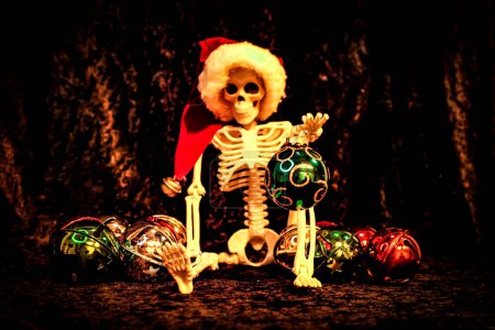 Foto de Mirando hacia adelante, este esqueleto sostiene una bola de Navidad mientras clasifica los adornos. - Imagen libre de derechos