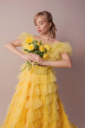 Foto de Hermosa joven rubia caucásica en vestido amarillo con rosas amarillas. Moda, felicidad, flores, concepto de estilo - Imagen libre de derechos