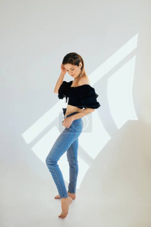 Photo for Beautiful slim young caucaisn woman in black blose and jeans on white background in photo studio - Royalty Free Image
