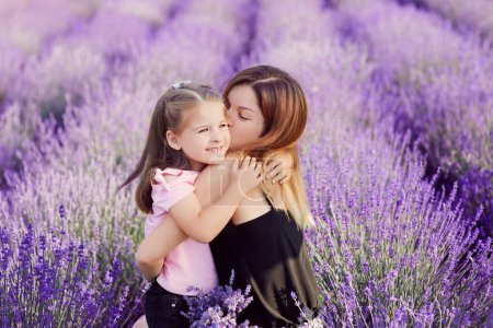 Photo for Caucasian mother kissing and cuddling her daughter in lavender field. Love, peace, family - Royalty Free Image