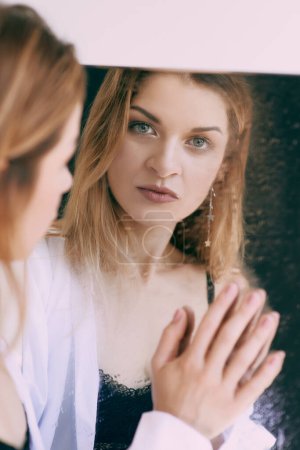 Foto de Hermosa mujer rubia caucásica en camisa blanca de pie junto al espejo. Salud, belleza, problemas mentales - Imagen libre de derechos