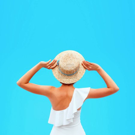 Foto de Ajuste la espalda de mujer caucásica en el traje de baño blanco sentado junto a la piscina (o el mar o el océano) en el sombrero de paja en el día de verano. Verano, relax, bienestar, concepto de recreación - Imagen libre de derechos