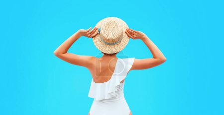 Téléchargez les photos : Placez le dos de la femme caucasienne dans le maillot de bain blanc assis près de la piscine (ou de la mer ou de l'océan) dans le chapeau de paille le jour d'été. Été, détente, bien-être, concept de loisirs - en image libre de droit
