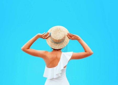 Foto de Ajuste la espalda de mujer caucásica en el traje de baño blanco sentado junto a la piscina (o el mar o el océano) en el sombrero de paja en el día de verano. Verano, relax, bienestar, concepto de recreación - Imagen libre de derechos