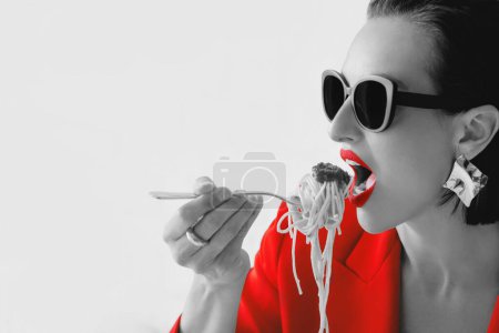 Téléchargez les photos : Portrait noir et blanc de la belle femme élégante à la mode avec des lunettes de soleil, veste rouge mangeant des pâtes spagetti. Alimentation, concept de mode - en image libre de droit