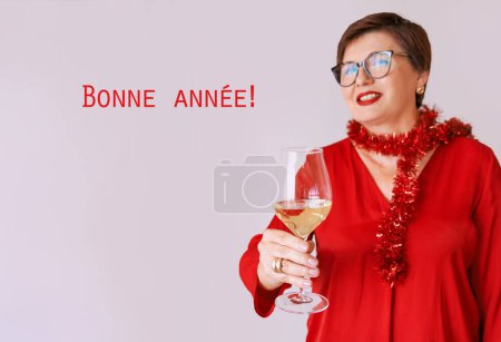 Téléchargez les photos : Élégante femme âgée mature en chemisier rouge avec un verre de vin blanc célébrant le nouvel an. Fun, fête, style de vie, alcool, concept de célébration - en image libre de droit