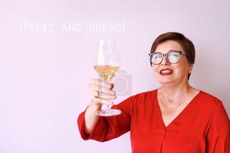 Foto de Mujer mayor madura con estilo en blusa roja con copa de vino blanco que celebra el año nuevo. Diversión, fiesta, estilo, estilo de vida, alcohol, concepto de celebración - Imagen libre de derechos