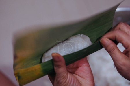 closeup of hands making lontong wrapped in banana leaves