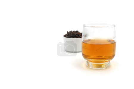 a glass of tea and a small cup of black tea leaves next to it
