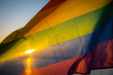 Téléchargez les photos : Drapeau LGBT sur fond de coucher de soleil au bord du lac. LGBT gay pride flag, lesbienne, gay, bisexuel, mouvements sociaux transgenres. Bonheur concept de liberté, amour couple de même sexe. Un drapeau agitant contre le vent a - en image libre de droit