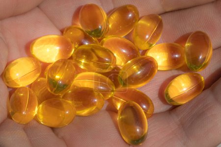 On the hand capsule with fish beer. Omega capsules in sunlight. Sunlight reflects fish oil in capsules. The right diet