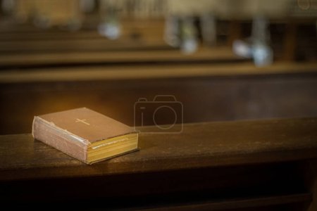 Foto de La Biblia en el banco de la iglesia. La palabra de Dios en un pequeño libro. Enfoque selectivo suave. Grano creado artificialmente para la imagen - Imagen libre de derechos