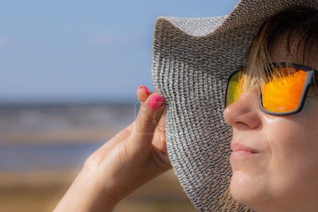 Téléchargez les photos : Une femme avec un chapeau et des lunettes de soleil prenait un bain de soleil sur la plage. Portrait avec mise au point douce. Été chaud, soleil et femme - en image libre de droit