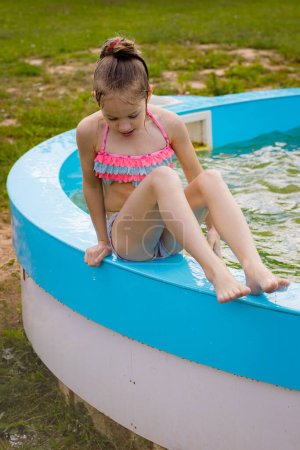 Photo for A little girl is swimming alone in the pool. A child by the pool of water. Child safety near water bodies - Royalty Free Image