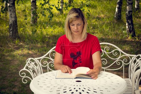 Foto de Una mujer con un libro en la mesa. Una mujer está leyendo un libro. Aprendizaje a distancia en casa - Imagen libre de derechos