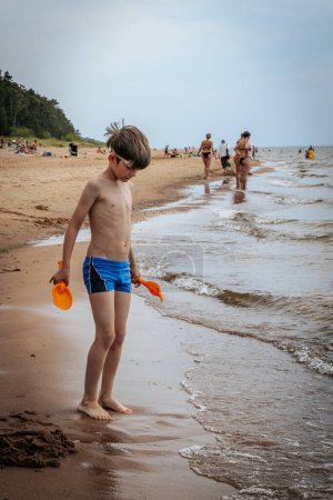 Un chico estaba jugando con arena en la orilla del mar. Un niño estaba jugando con arena marina en la orilla arenosa del mar. Enfoque selectivo suave