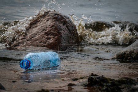 Eine Plastikflasche an den Felsen am Ufer des Meeres. Müll am Strand. Mikroplastik an den Küsten. Weiche selektive Fokussierung
