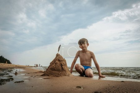 Photo for A boy made a pyramid out of sand on the seashore. A child was playing with sea sand on the sandy shore of the sea. Soft selective focus - Royalty Free Image