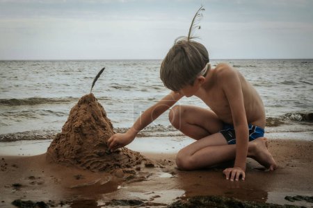 Téléchargez les photos : Un garçon a fait une pyramide de sable sur le bord de la mer. Un enfant jouait avec le sable marin sur le rivage sablonneux de la mer. Concentration sélective douce - en image libre de droit