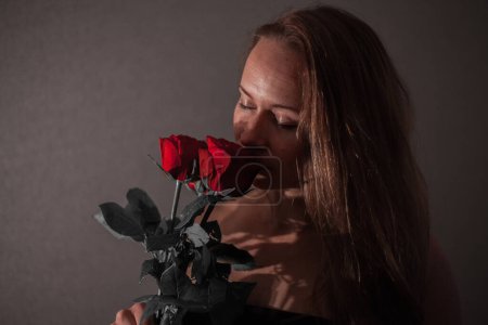 Foto de Mujer con rosas rojas. Una joven en la oscuridad. - Imagen libre de derechos
