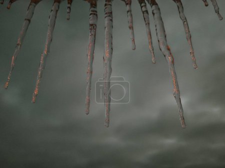The serene winter landscape features glistening icicles hanging against a dusky sky. The snow-covered ground and trees are illuminated by distant lights. The overall atmosphere is chilly and calm.