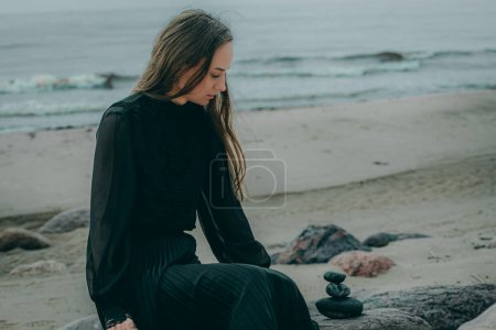 Woman by the sea in dark clothes with long hair on blurred natural background.