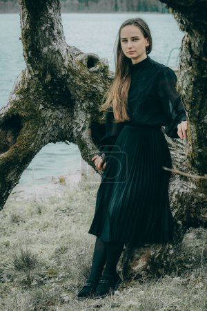 Eine Frau in schwarzem Mantel steht am Ufer eines Sees