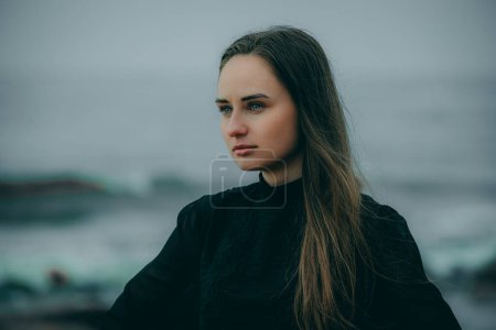 Woman by the sea in dark clothes with long hair on blurred natural background.