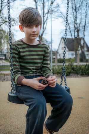 A boy is sitting on a swing. Smiling happy child