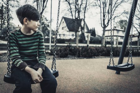 Junge sitzt traurig auf der Schaukel. Ein einsames Kind wartet auf einen Freund. Ein deprimiertes und trauriges Kind