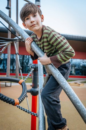 child rested in the childrens playground. The boy was hanging on the bars. Smiling happy child