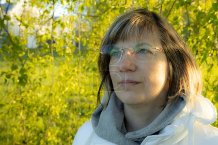 Mujer con gafas transparentes bajo hojas verdes de abedul