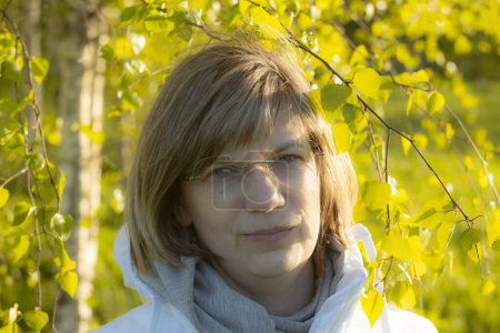 Frau mit durchsichtiger Brille unter grünen Birkenblättern