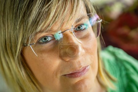Téléchargez les photos : Gros plan portrait d'une femme portant des lunettes, mettant en valeur ses yeux bleus et ses traits faciaux. Elle a les cheveux blonds courts et porte un haut vert. L'image est détaillée, capturant les expressions subtiles - en image libre de droit