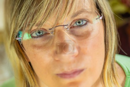 Téléchargez les photos : Portrait d'une femme portant des lunettes, mettant en valeur ses yeux bleus et ses traits faciaux. Elle a les cheveux blonds courts et porte un haut vert. L'image est détaillée, capturant les expressions subtiles - en image libre de droit