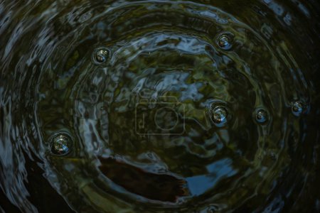 une gouttelette d'eau créant des ondulations dans l'eau sombre. Les éclaboussures et les cercles concentriques sont capturés en détail, mettant en évidence la dynamique des fluides et le mouvement.
