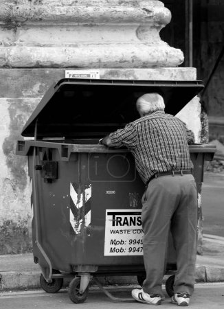 Téléchargez les photos : Mendiant fouilles dans les ordures de la ville - en image libre de droit